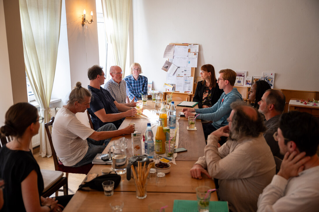 Minsiterin Meier und Teilnehmende Bürger/innen sitzen an einem Tisch und diskutieren