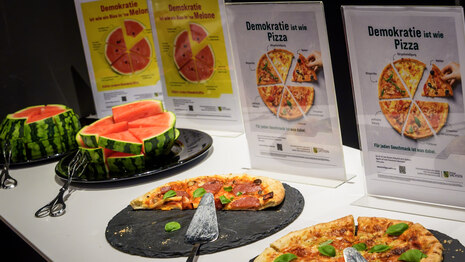 Melone und Pizza am Buffet mit Pizza- und Melonen-Plakaten im Hintergrund